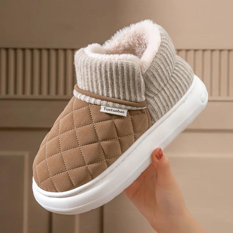 Brown quilted slipper with white sole held by a hand against a neutral background