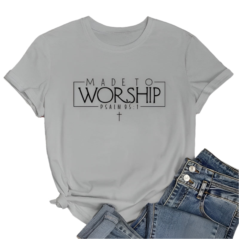 Gray t-shirt with 'Made to Worship' text on a wooden surface with jeans and sunglasses.