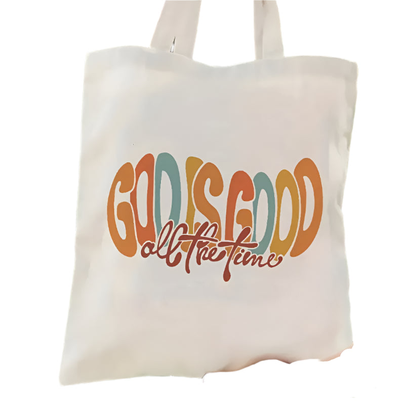 Tote bag with 'God is Good all the time' text held by a person outdoors.