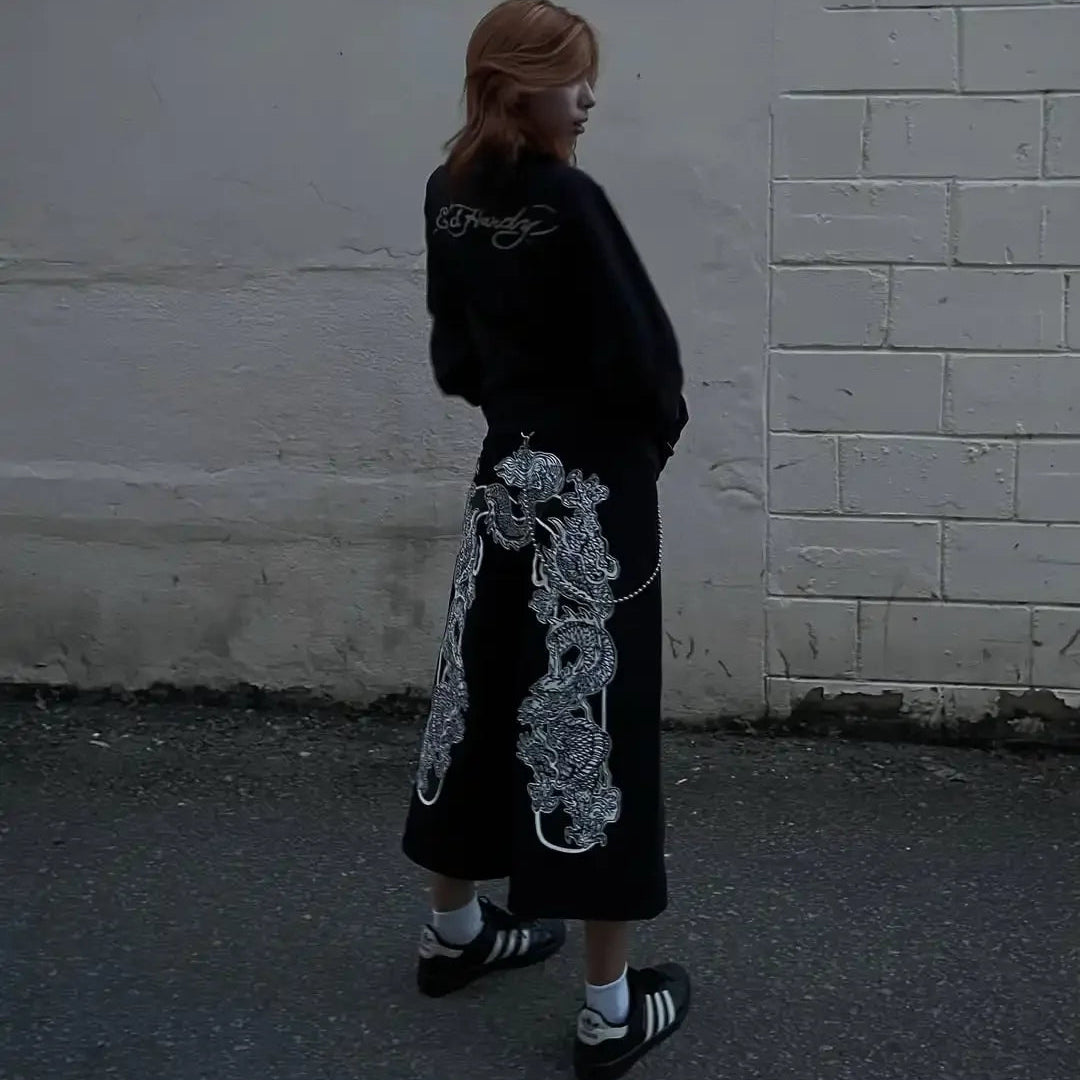 Person wearing a black outfit with white floral designs against a white wall.