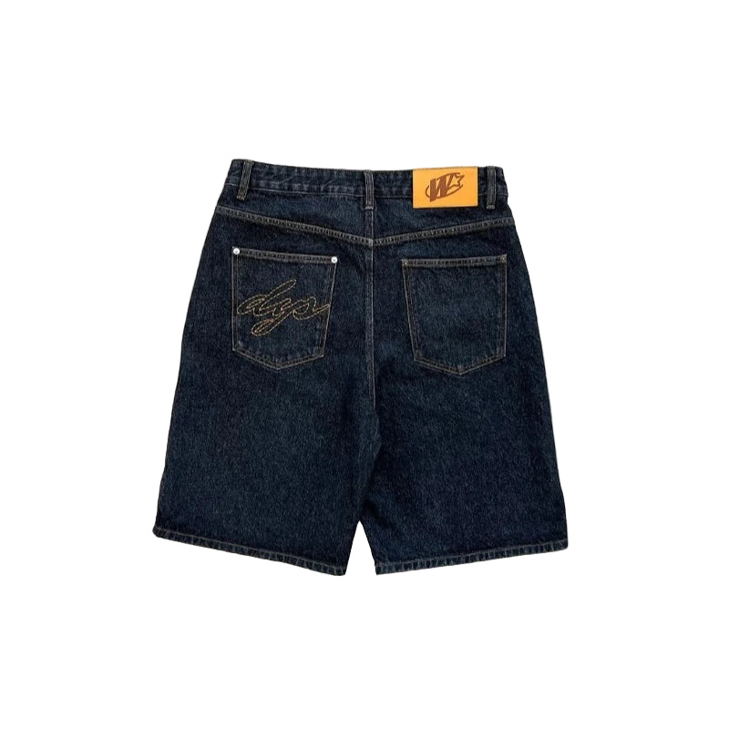 Black denim shorts with brand logo on a gray concrete surface