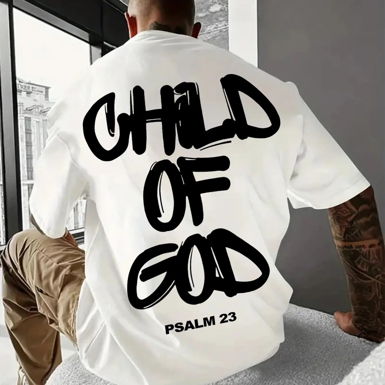 Person wearing a white t-shirt with 'Child of God' text on the back, sitting indoors.