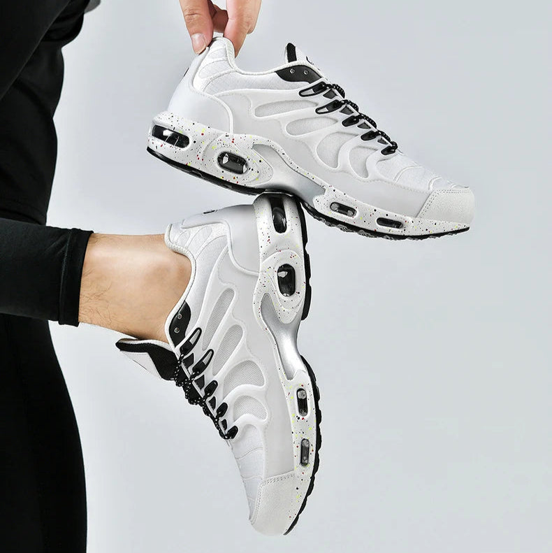 White sneakers with black accents held by a person against a light gray background