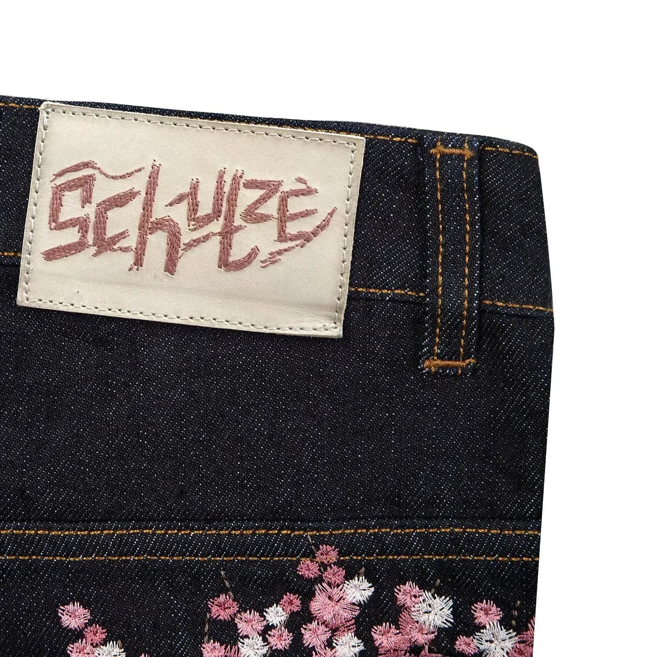 Close-up of a denim product with a brand label and floral embroidery.