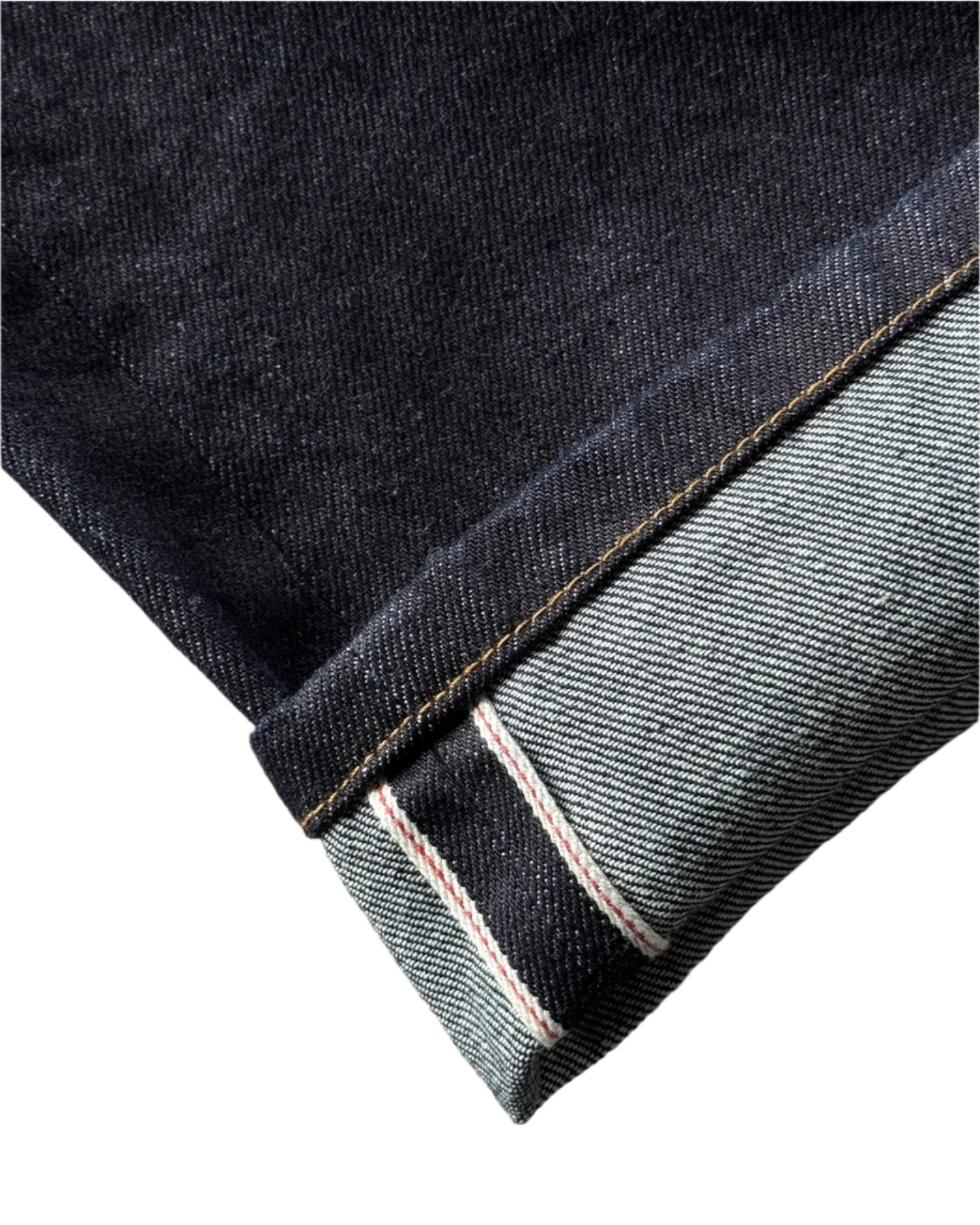 Close-up of a folded denim fabric with a visible selvedge on a concrete surface.