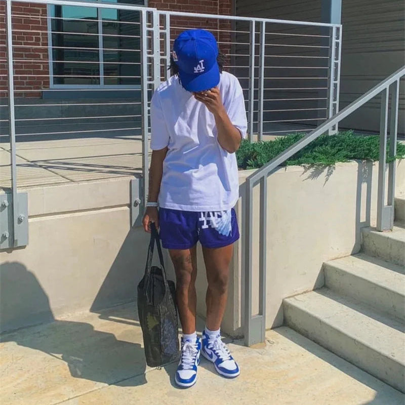 Person wearing a white t-shirt, blue shorts, and a blue cap, standing outdoors.