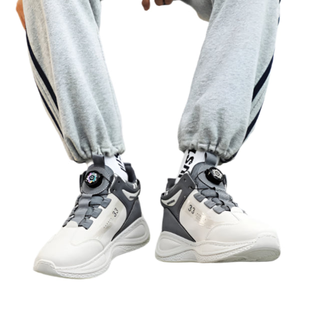 Person wearing a gray sweatshirt, light gray pants, and white sneakers with black accents sitting on a chair.