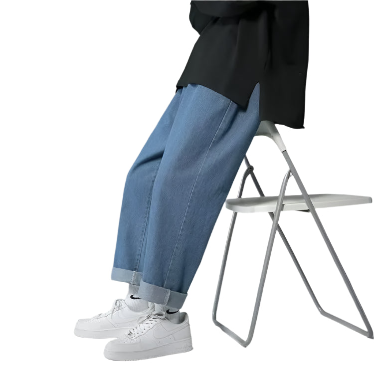 Person wearing blue jeans and white sneakers sitting on a chair against a gray background