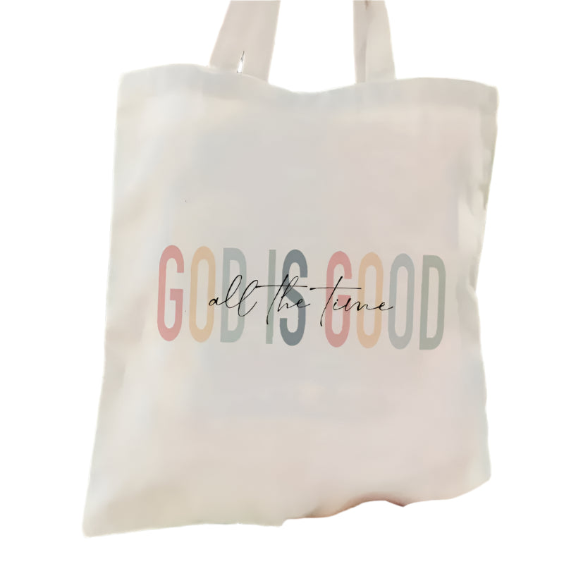 Tote bag with 'GOD IS GOOD all the time' text held by a person against a green background