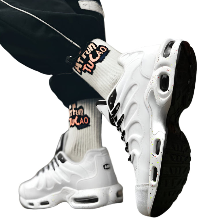 White sneakers with black soles worn by a person, with a blurred background.