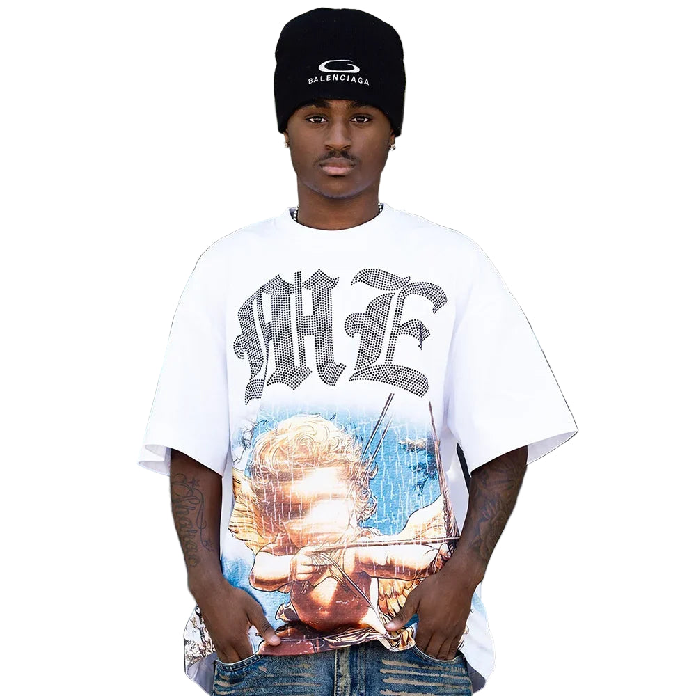Person wearing a white t-shirt with graphic design and text, standing in front of a blurred background with greenery.