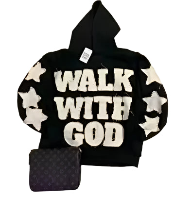 Black hoodie with 'Walk With God' text and star patterns on a tiled floor, next to a Louis Vuitton handbag.