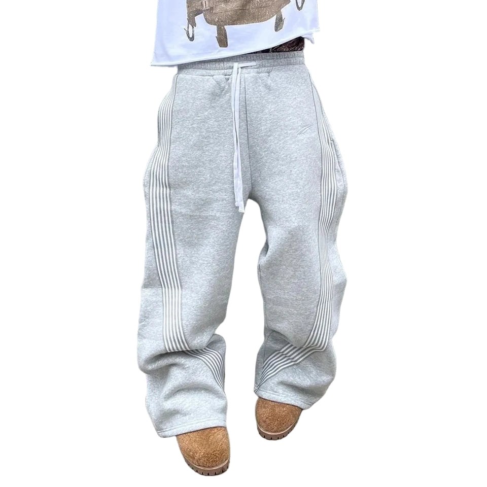 Person wearing a white graphic t-shirt and gray sweatpants against a light gray wall.