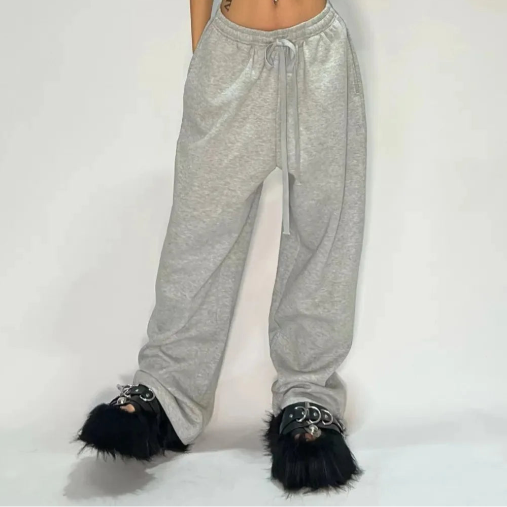 Person wearing gray sweatpants with black fur-trimmed shoes on a plain background