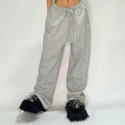 Person wearing gray sweatpants with black fur-trimmed shoes on a plain background