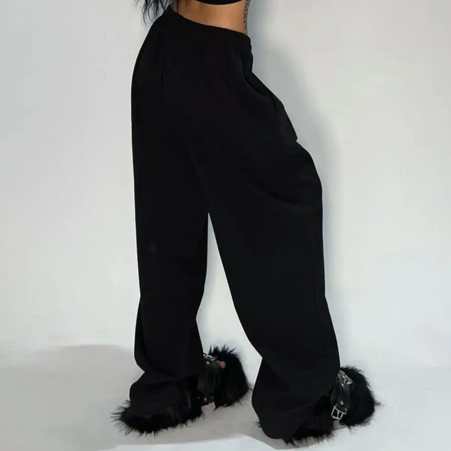 Person wearing a black outfit with fluffy shoes on a plain background