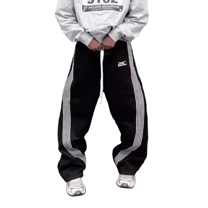 Person wearing a white sweatshirt with text and black pants with white stripes against a gray wall.