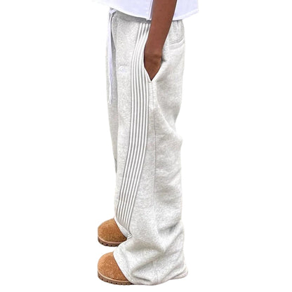 Person wearing white pants with pleated sides against a gray wall.