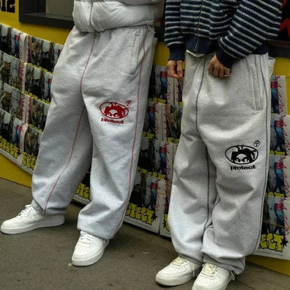 Two people wearing gray sweatpants with logos in front of a colorful store display.