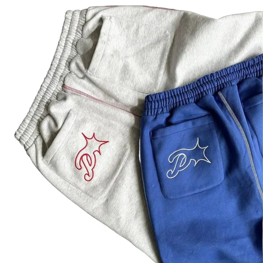 Gray and blue sweatpants with embroidered logos on a dark surface