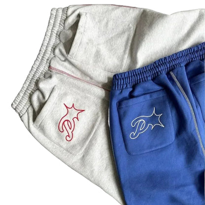 Gray and blue sweatpants with embroidered logos on a dark surface