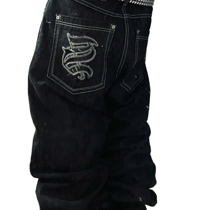 Black pants with a logo on the pocket worn by a person, standing indoors.