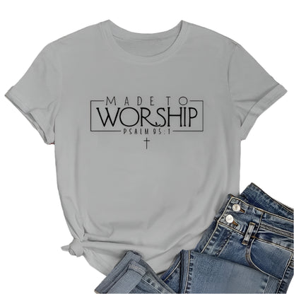 Gray t-shirt with 'Made to Worship' text on a wooden surface with jeans and sunglasses.