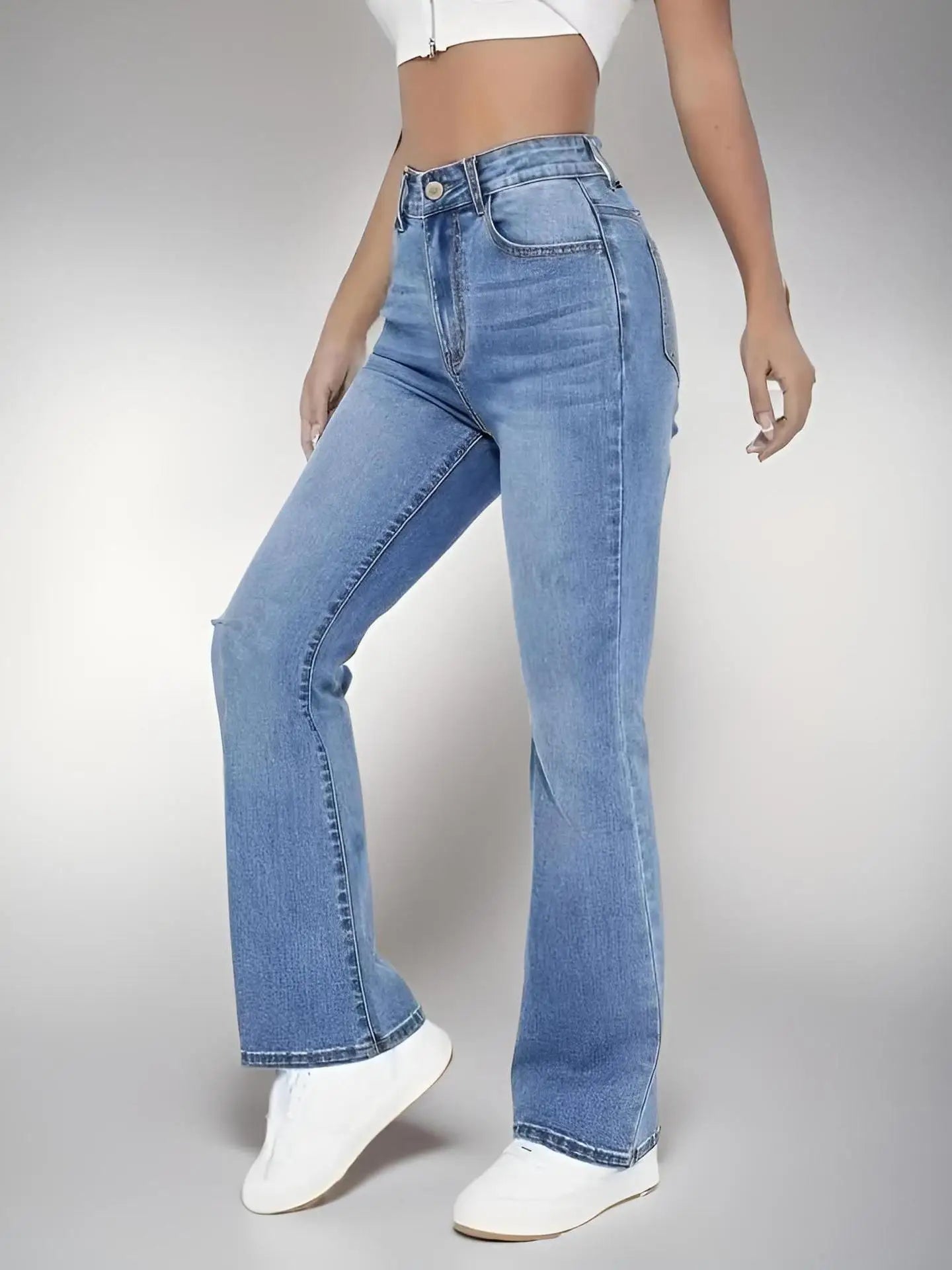 Person wearing blue jeans and white shoes on a gray background