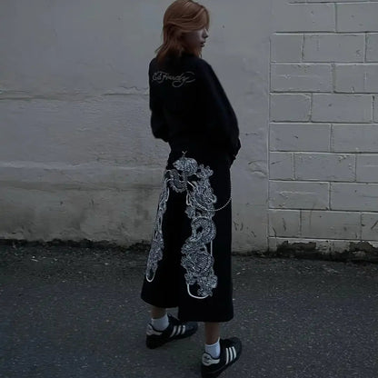 Person wearing a black outfit with white floral designs against a white wall.