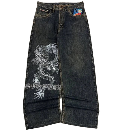 Dark blue jeans with a white dragon design on a gray surface, featuring brand logos.