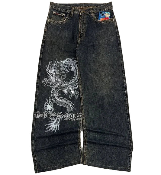 Dark blue jeans with a white dragon design on a gray surface, featuring brand logos.