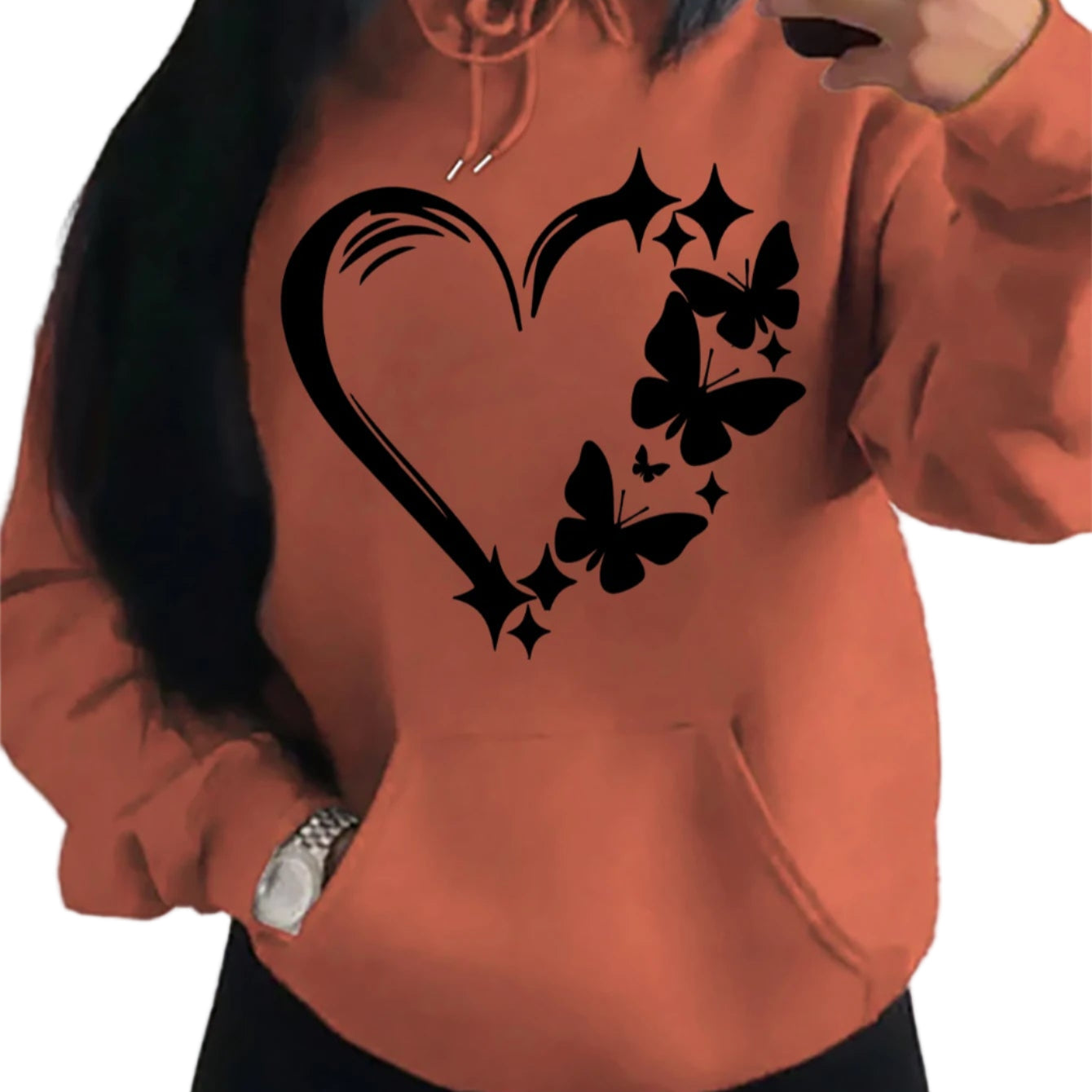 Person wearing an orange hoodie with black heart, butterfly, and star design.