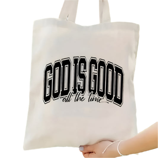 Tote bag with 'GOD IS GOOD all the time' text held by a person against a green background