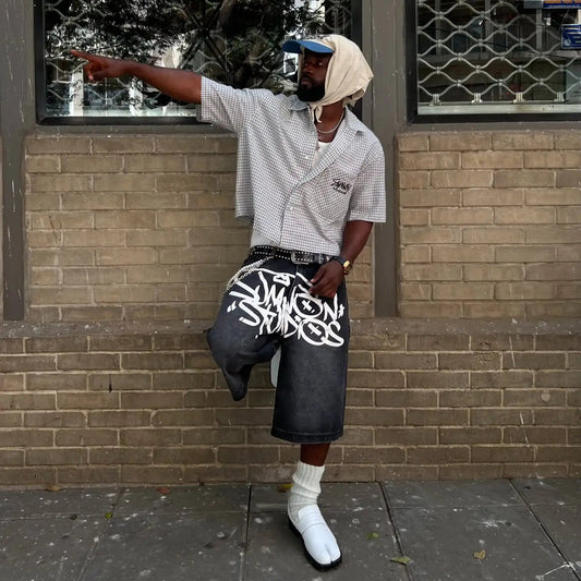 Person standing against a brick wall wearing a checkered shirt, cap, and shorts with text.