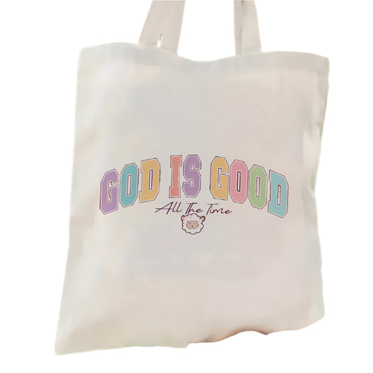 Tote bag with 'God is Good All the Time' text held by a person outdoors.