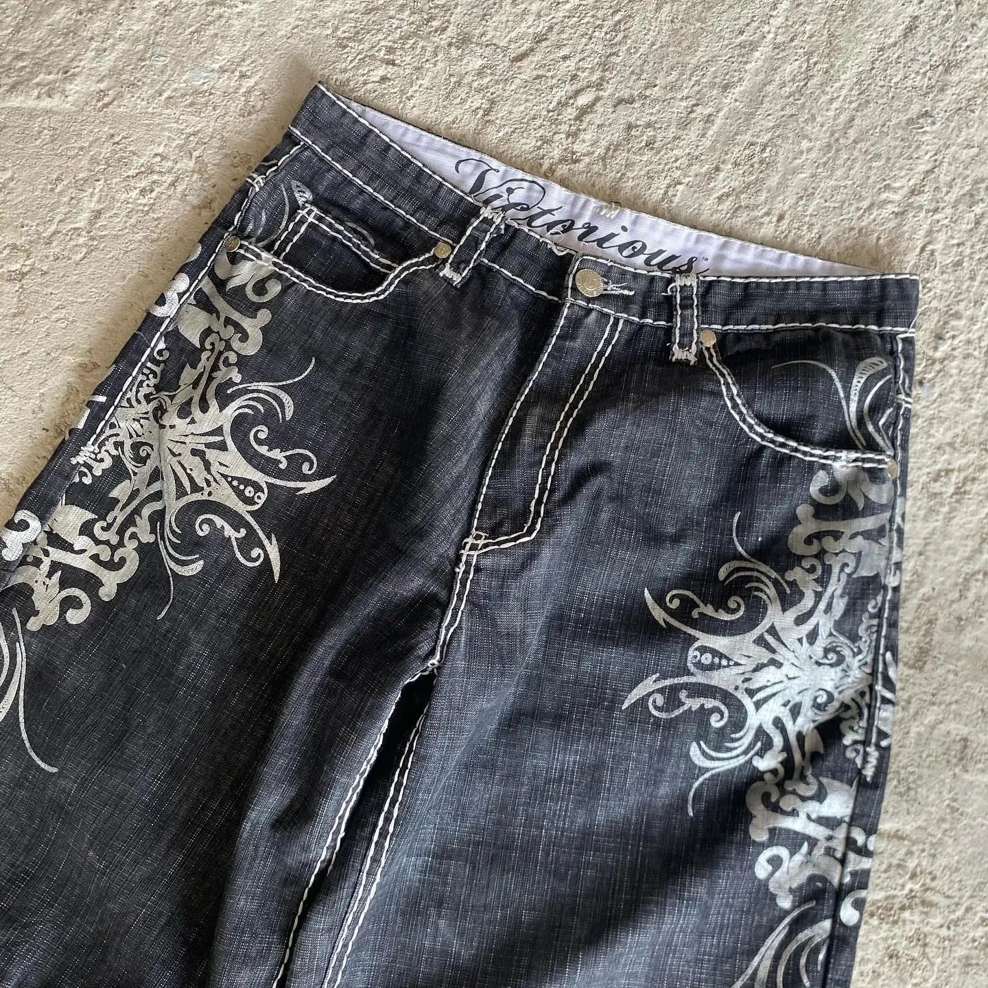 Black jeans with white floral patterns on a beige surface