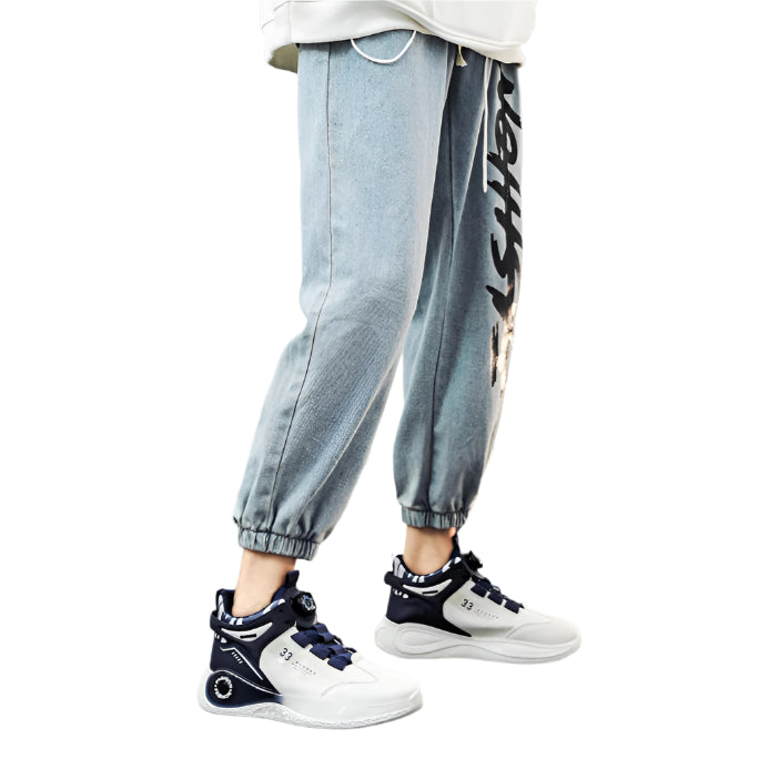 Person wearing a white hoodie, light blue jeans with text, and black and white sneakers on a gray floor.