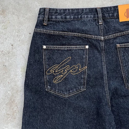 Dark blue denim jeans with a brand logo on the back pocket against a concrete floor background
