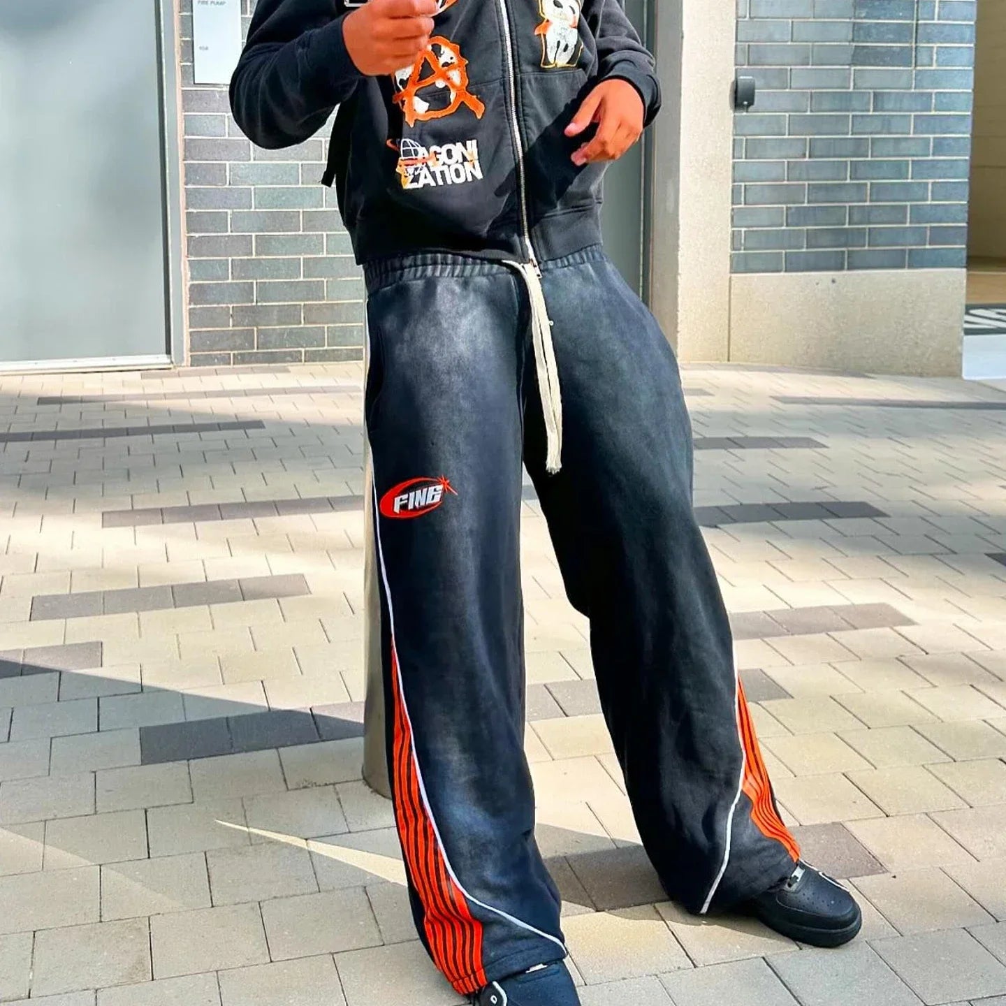Person wearing a dark hoodie and blue pants with red stripes on a paved sidewalk.