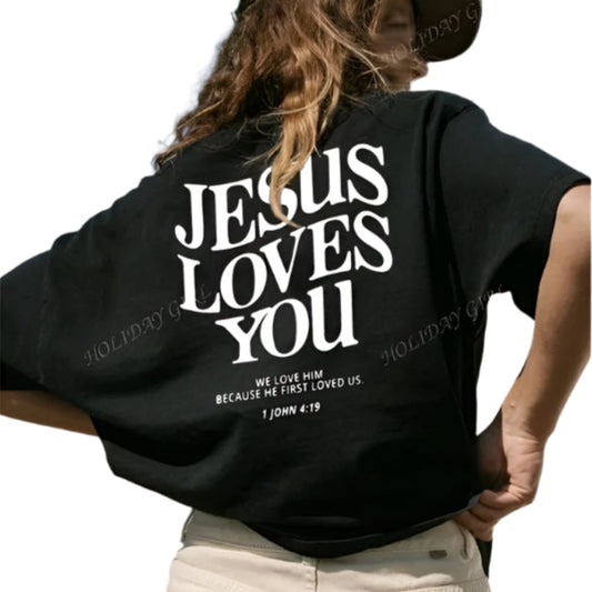 Person wearing a black t-shirt with 'Jesus Loves You' text against a clear blue sky.
