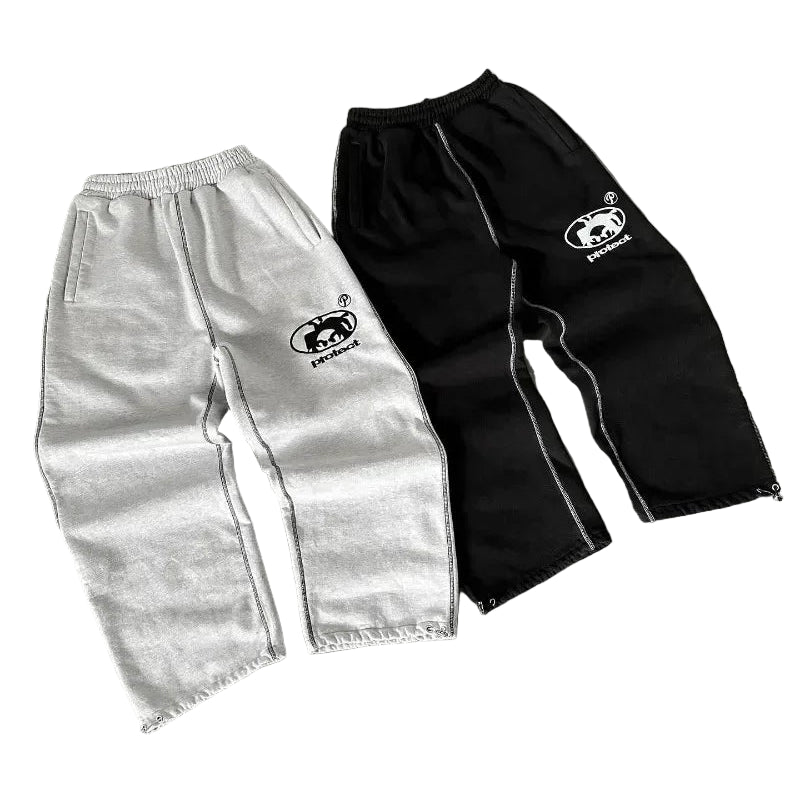 Two pairs of pants, one gray and one black, with a logo on a gray surface.