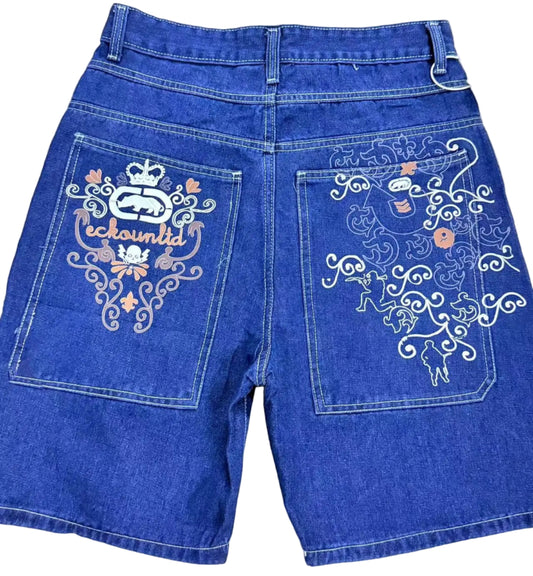 Blue denim shorts with decorative patterns on the back pockets, on a white floor.