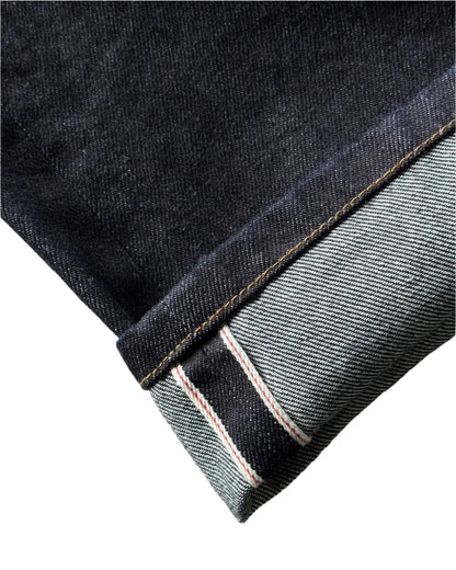 Close-up of a folded denim fabric with a visible selvedge on a concrete surface.