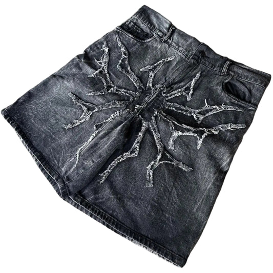 Black denim shorts with tree branch design on a concrete surface