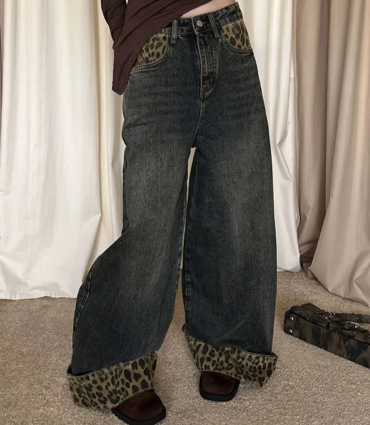 Person wearing wide-leg jeans with leopard print cuffs against a neutral curtain background