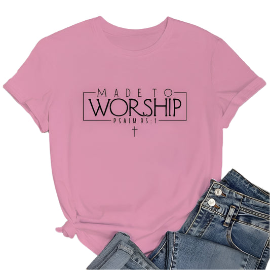 Pink t-shirt with 'Made to Worship' text on a wooden surface with jeans and sneakers.