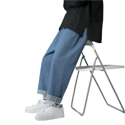 Person wearing blue jeans and white sneakers sitting on a chair against a gray background