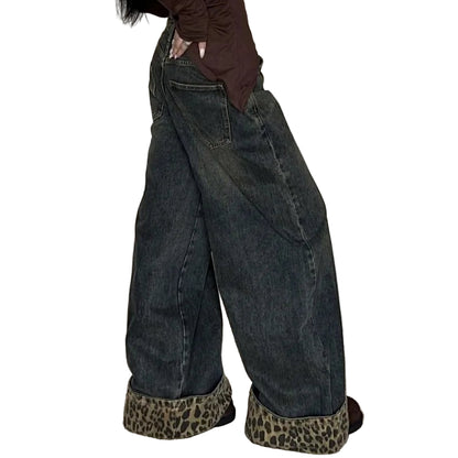 Person wearing a brown long-sleeve top and dark jeans with leopard print shoes against a white curtain background.
