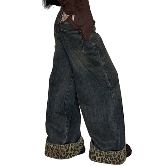 Person wearing a brown long-sleeve top and dark jeans with leopard print shoes against a white curtain background.