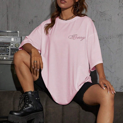 Person wearing a pink oversized t-shirt with text, sitting on a couch with a vintage boombox.